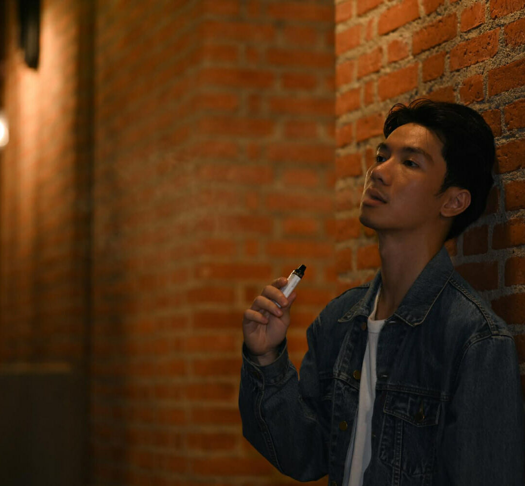 男子吸烟与电子烟站立夜间城市与模糊夜间路灯背景